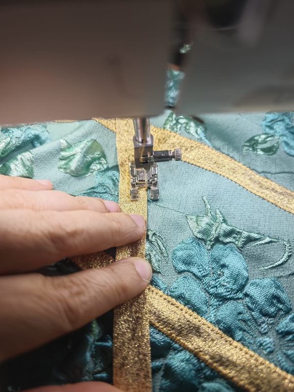 Una mano guida il jacquard di Frammenti e Velocità sotto il piedino della macchina da cucire